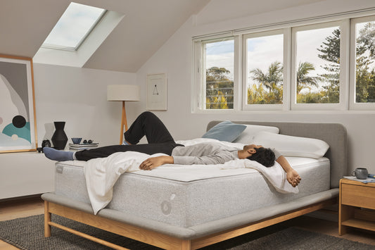 A man lies on a Koala mattress on a Koala bed frame in a bright, airy bedroom.