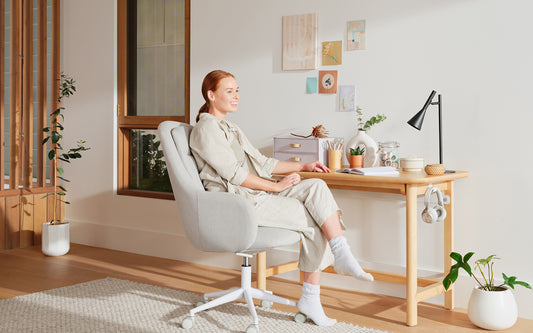 A smiling woman sits at her home office desk in her bright and clean home