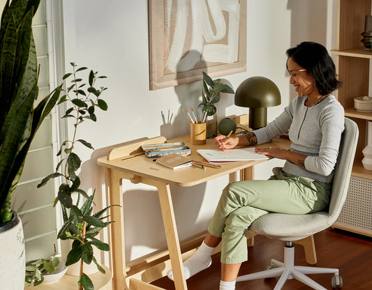 A smiling woman sits at her home office desk in her bright and clean home office workspace