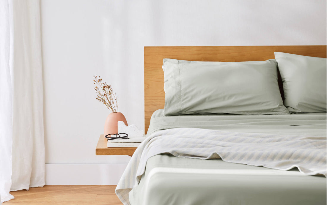 A close-up image of the corner of a bed with beautiful soft sheets, timber headboard and side table in a clean, modern bedroom