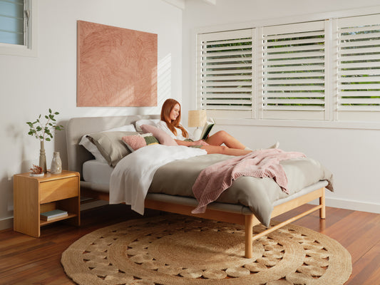 A woman reads a book on a Koala mattress and Koala Paddington Bed Base in a well-lit bedroom.