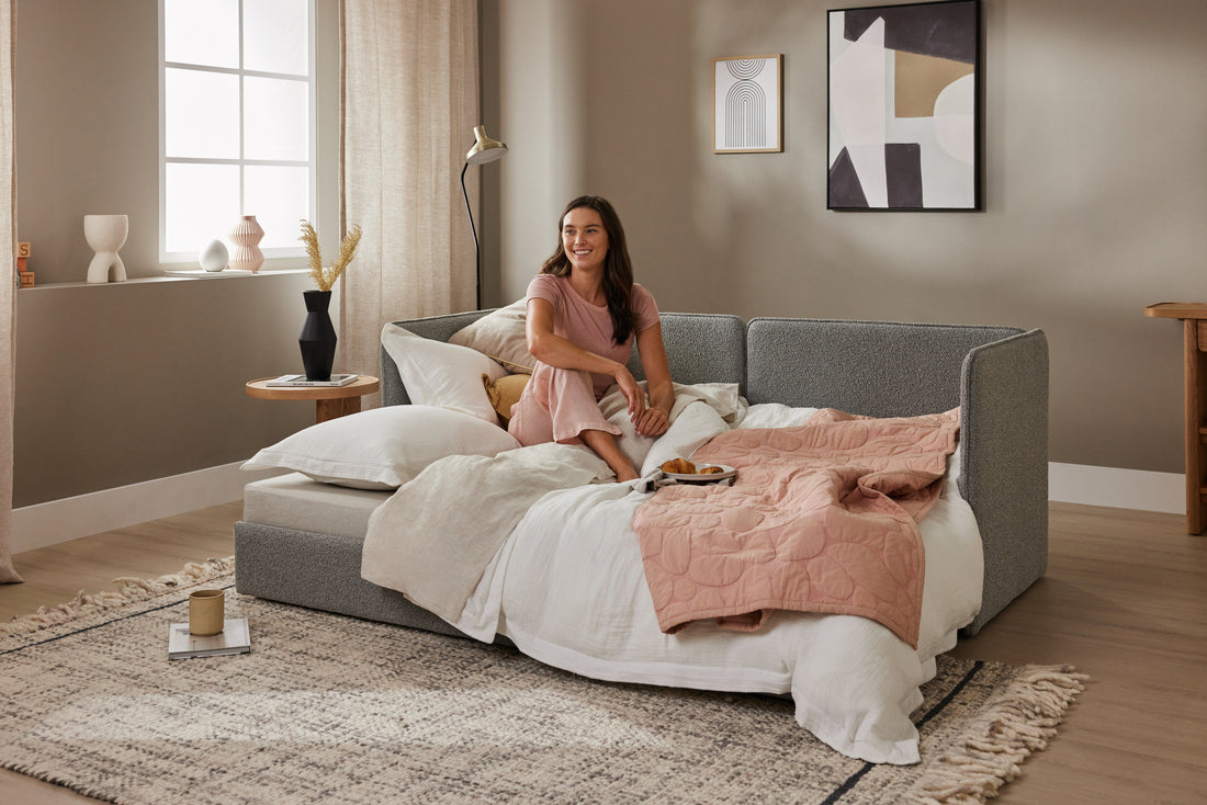 A woman smiles as she sits on her Koala Stunner sofa bed with storage in a large lounge room