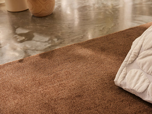 Brown rug on polished concrete floor, near two beige vases; corner of a white patterned cushion visible.
