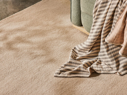 Beige carpet with a striped grey and beige blanket draped over a green sofa in a softly lit room.