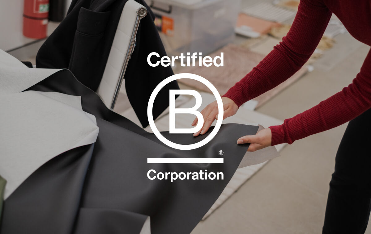 A person arranges black and white fabric on a table, with a "Certified B Corporation" logo overlay. An office is visible in the background.
