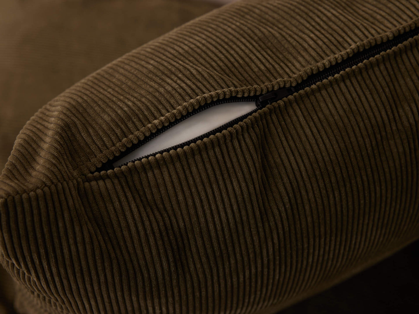 Close-up of a brown corduroy cushion with a visible black zipper partially open, revealing white inner lining.