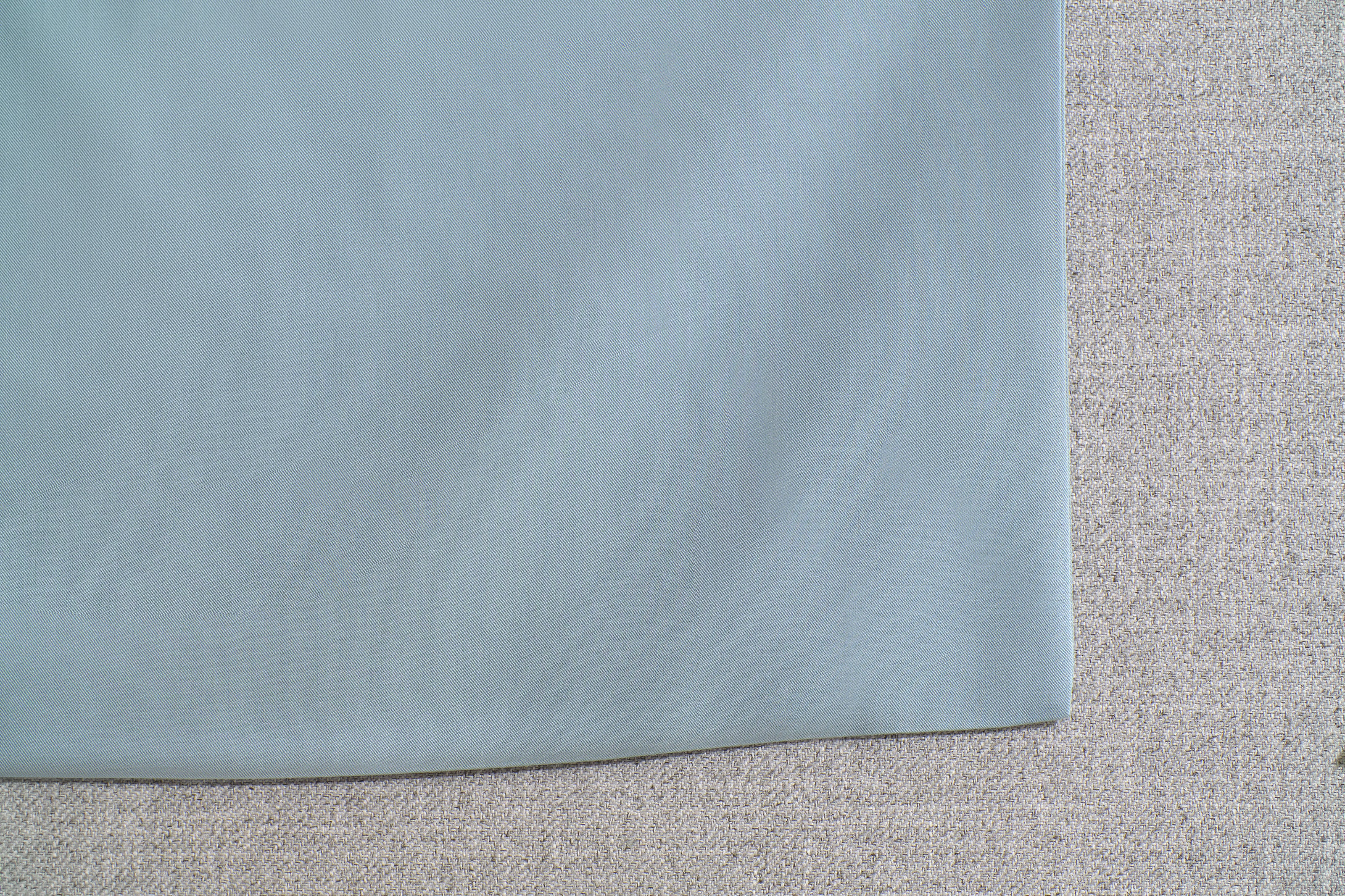 Close-up of a light grey fabric overlaid on a textured beige surface, possibly showing upholstery or textile material.