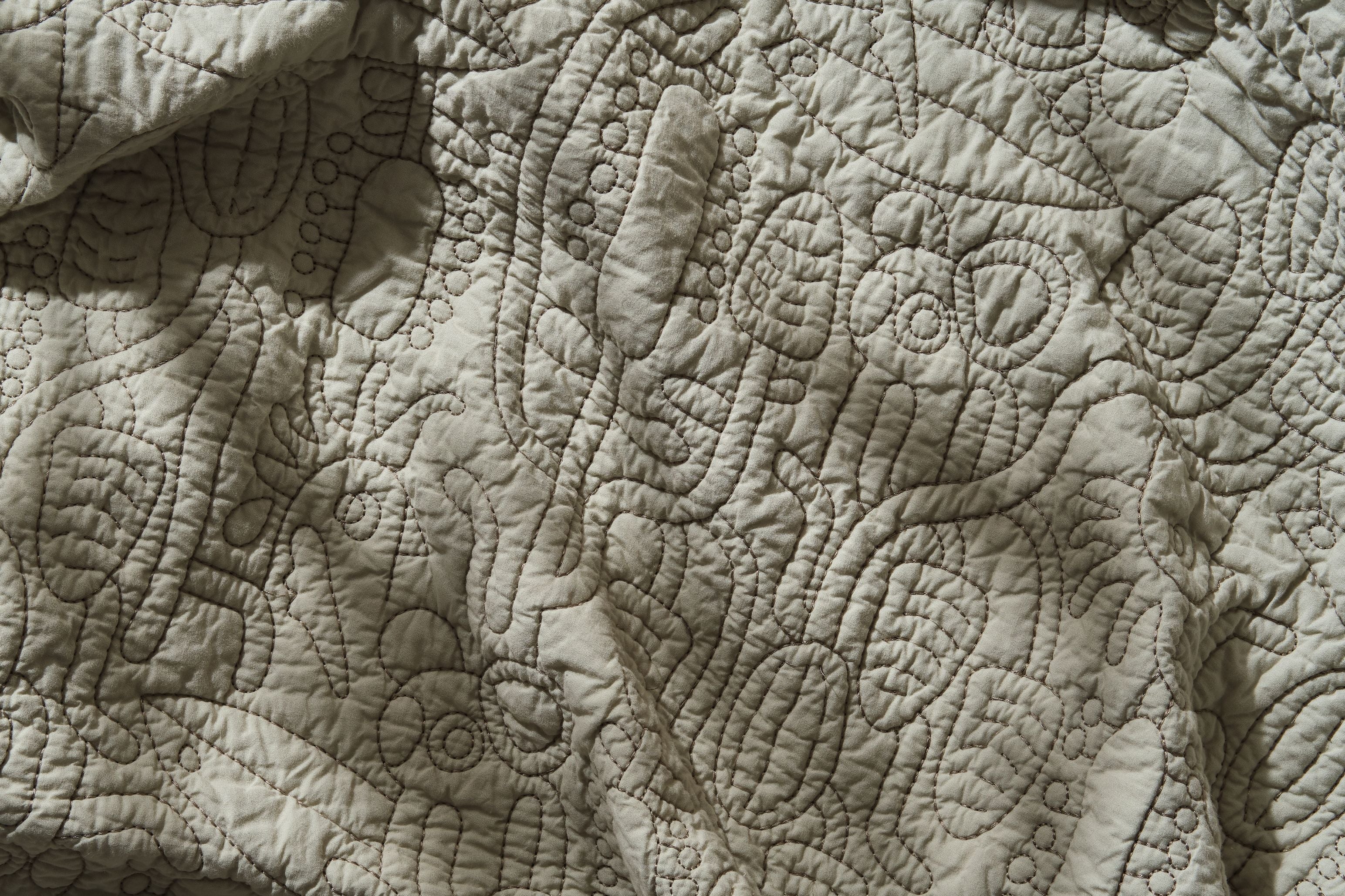 Close-up of a textured quilt featuring intricate stitching with abstract patterns on light grey fabric.