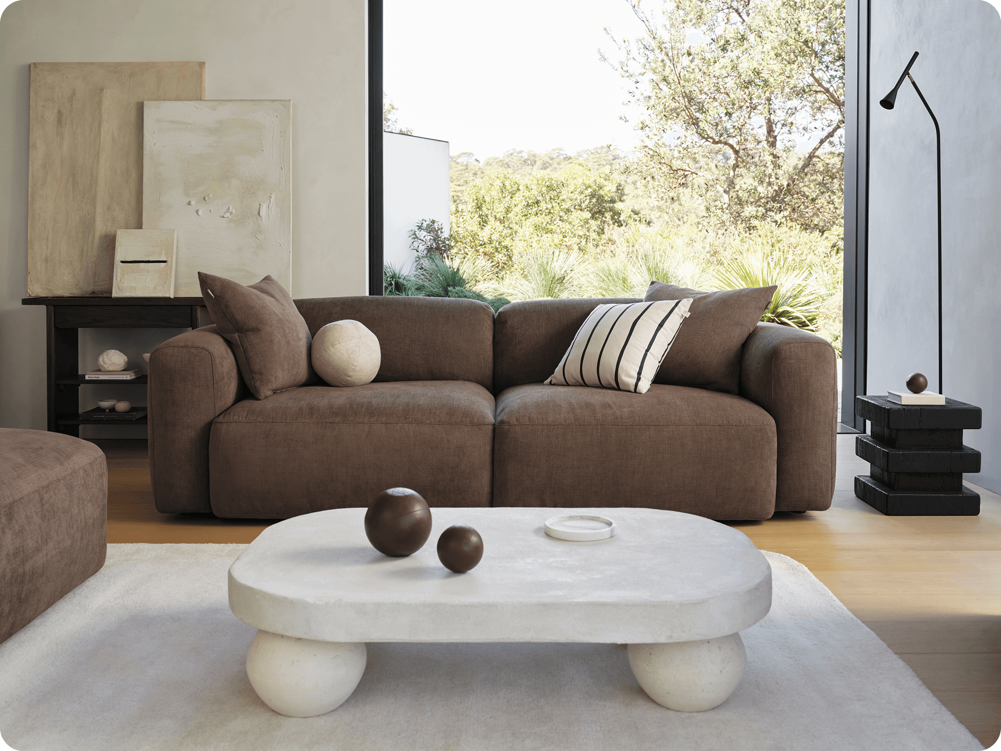 Cozy brown sofa with mixed pillows in a sunlit living room featuring a low stone coffee table and modern decor