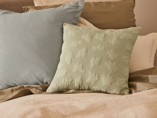Beige bedding with sage green and light blue accent cushions, featuring subtle textured patterns.