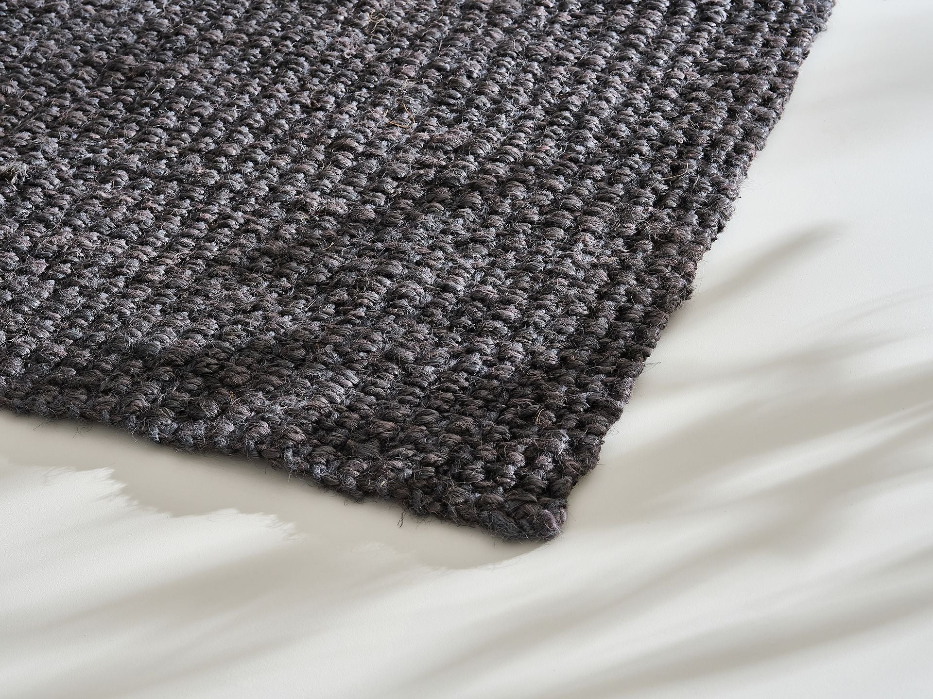 Close-up of a textured dark grey rug on a light floor, showcasing detailed weave pattern and subtle shadows.