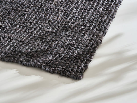 Close-up of a textured dark grey rug on a light floor, showcasing detailed weave pattern and subtle shadows.