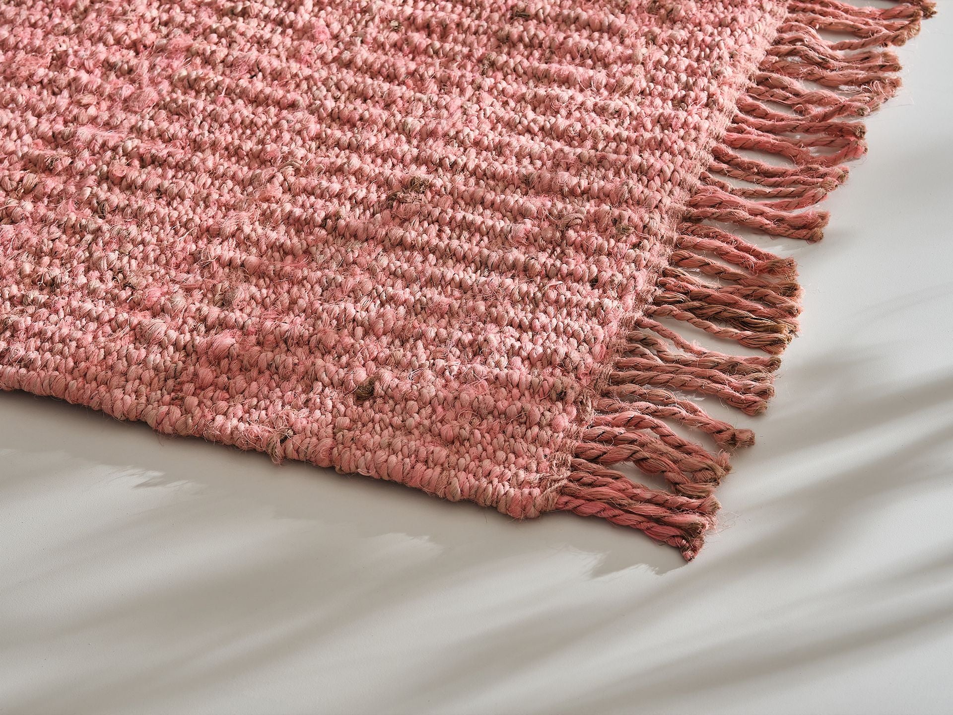 Close-up of a textured pink woven rug with fringed edges on a smooth white surface.