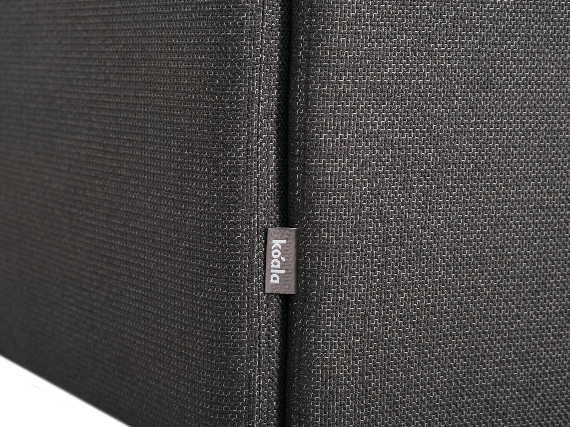 Close-up of dark grey textured fabric with a small "koala" tag, likely part of a sofa or cushion.