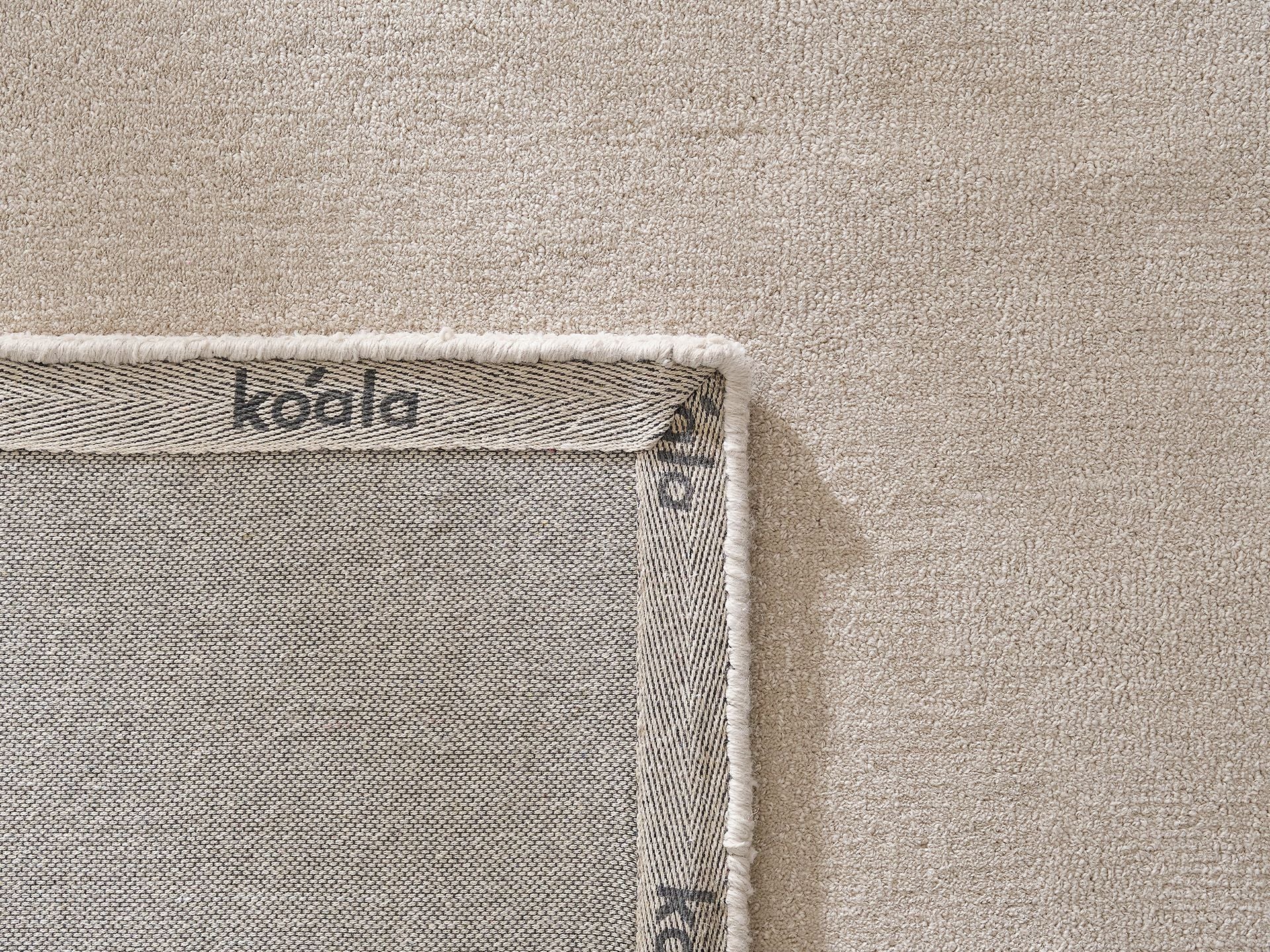 Close-up of a beige fabric with the corner of a grey mat, label reading "koala". Textile texture is visible.