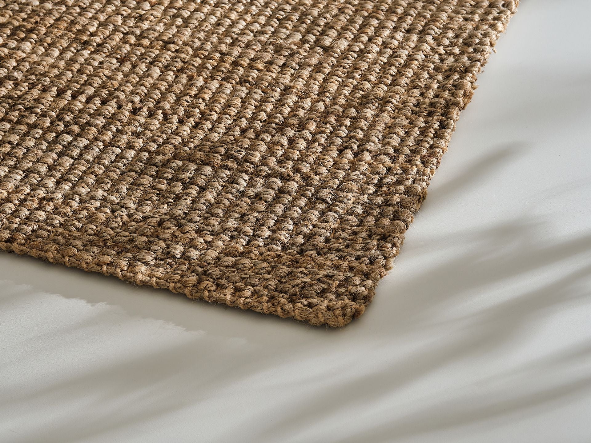 Close-up of a woven beige textured jute rug corner on a light grey floor. Natural fibre home decor accent.