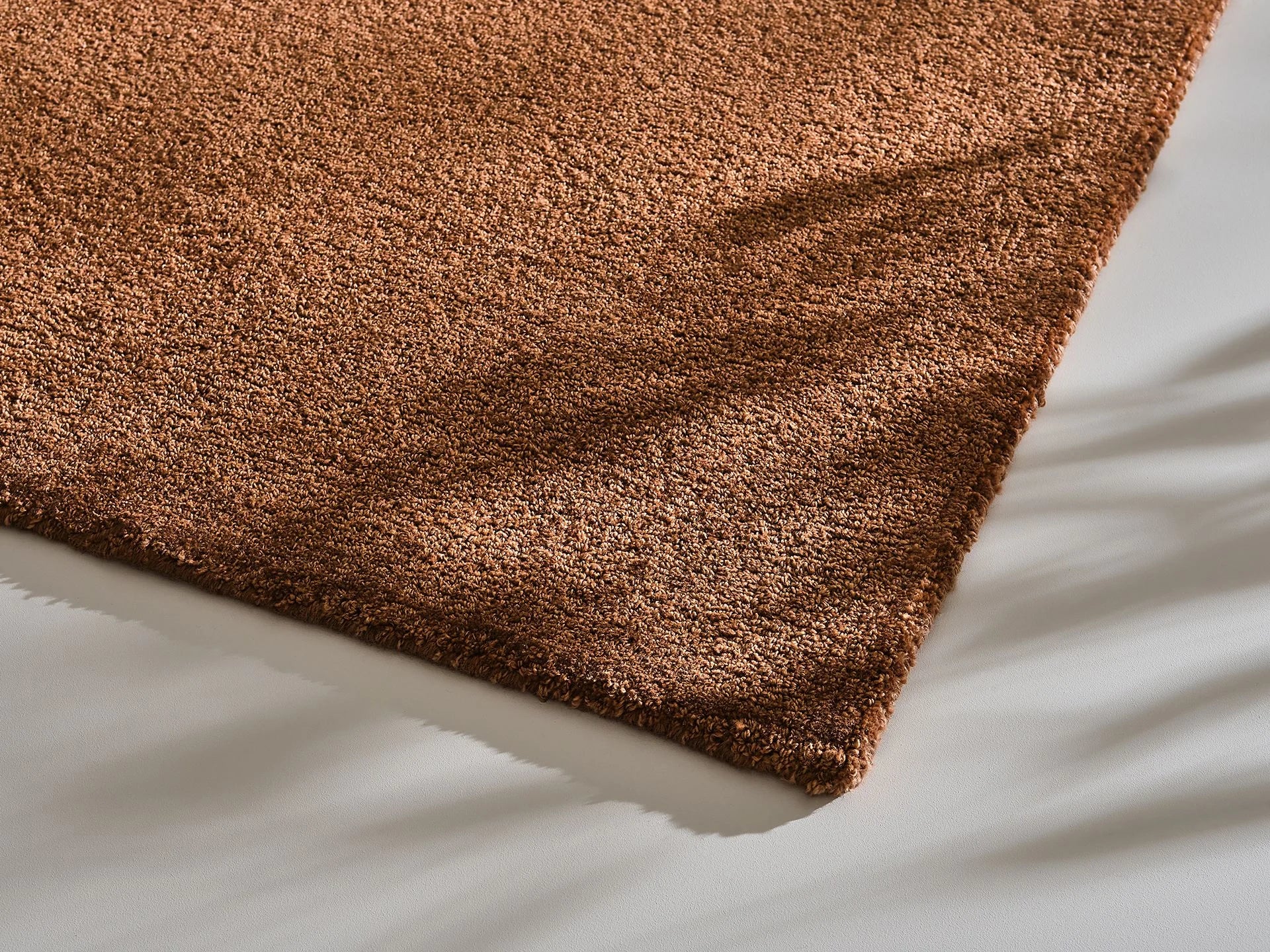Close-up of a brown textured rug corner on a smooth light grey floor.