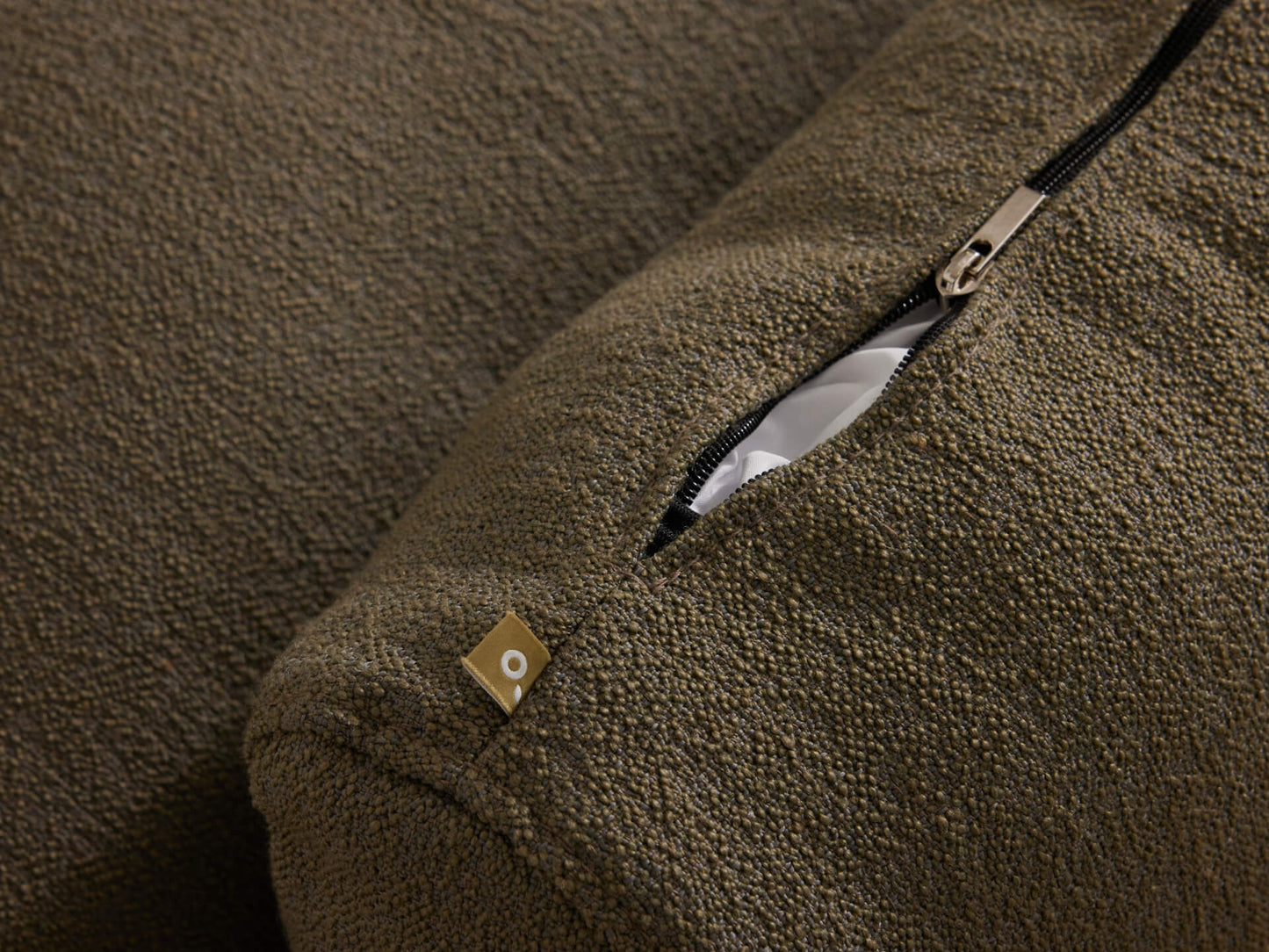 Close-up of a textured dark green cushion with a visible black zipper and small square tag. Ideal for living room furniture styling.