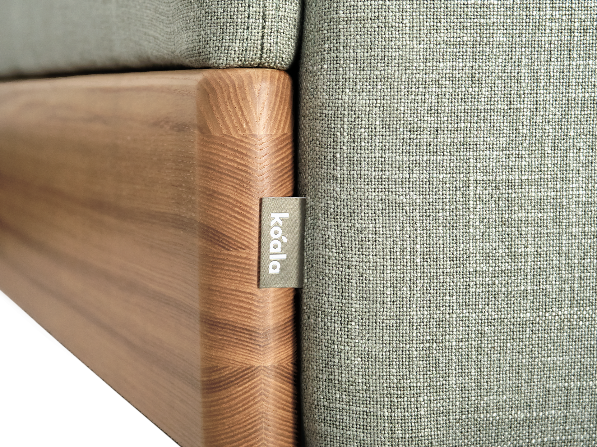 Close-up of a grey fabric couch with a wooden frame. A small tag with "koala" is attached to the side.