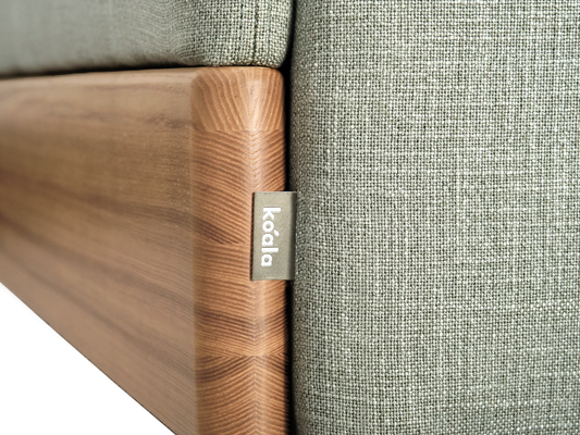 Close-up of a light grey fabric sofa with a wooden frame and a small metal label.