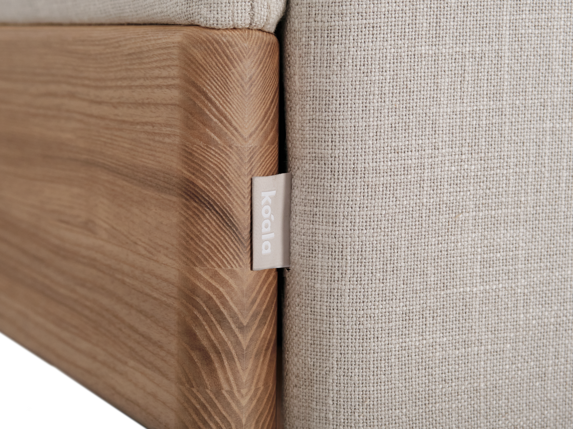 Close-up of a light brown fabric sofa with a natural wood frame, featuring a small tag with "Koala" written on it.