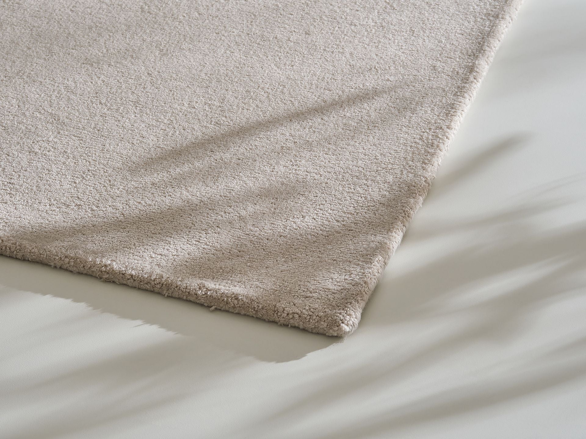 Close-up of a light grey textured rug corner on a smooth surface, with soft shadows cast across both.