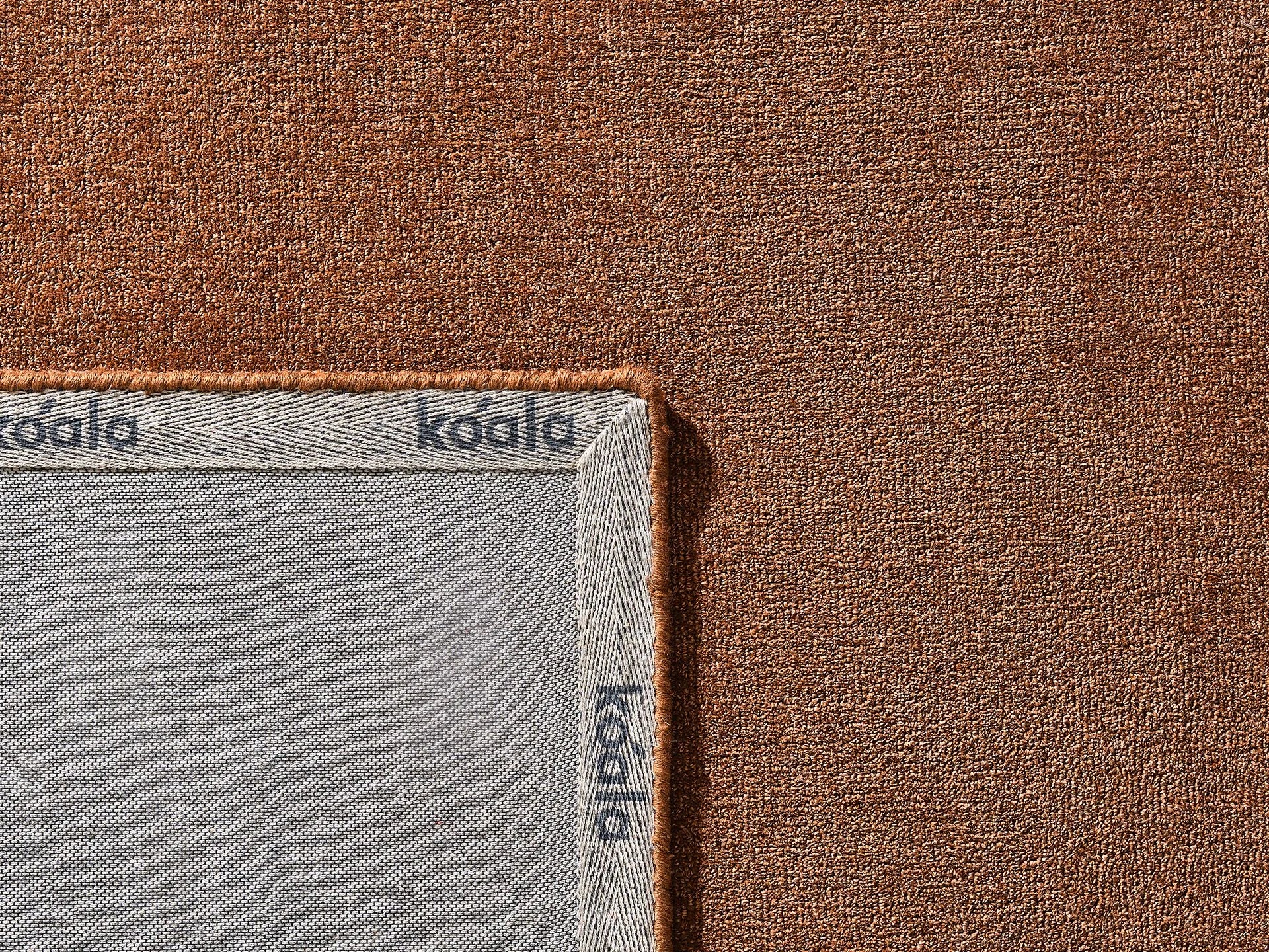 Close-up of brown textured fabric with a grey underside, partially folded to reveal "koala" branding. Ideal for upholstery or home decor.