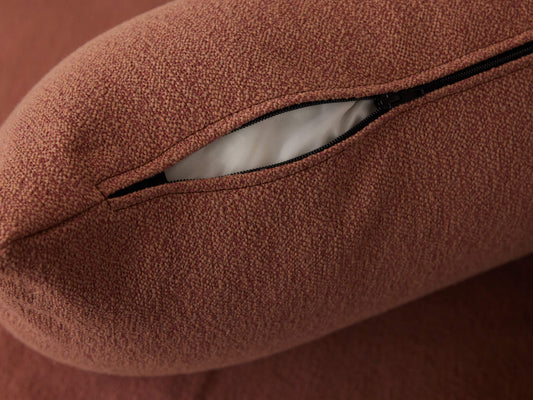 Close-up of a zipped opening on a rust-coloured fabric cushion cover, revealing white inner lining.