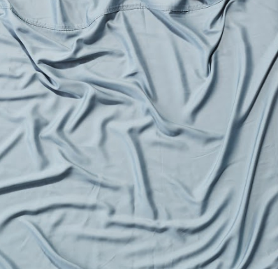 Light grey fabric with smooth, flowing folds and creases, texture accentuated by subtle shadows.