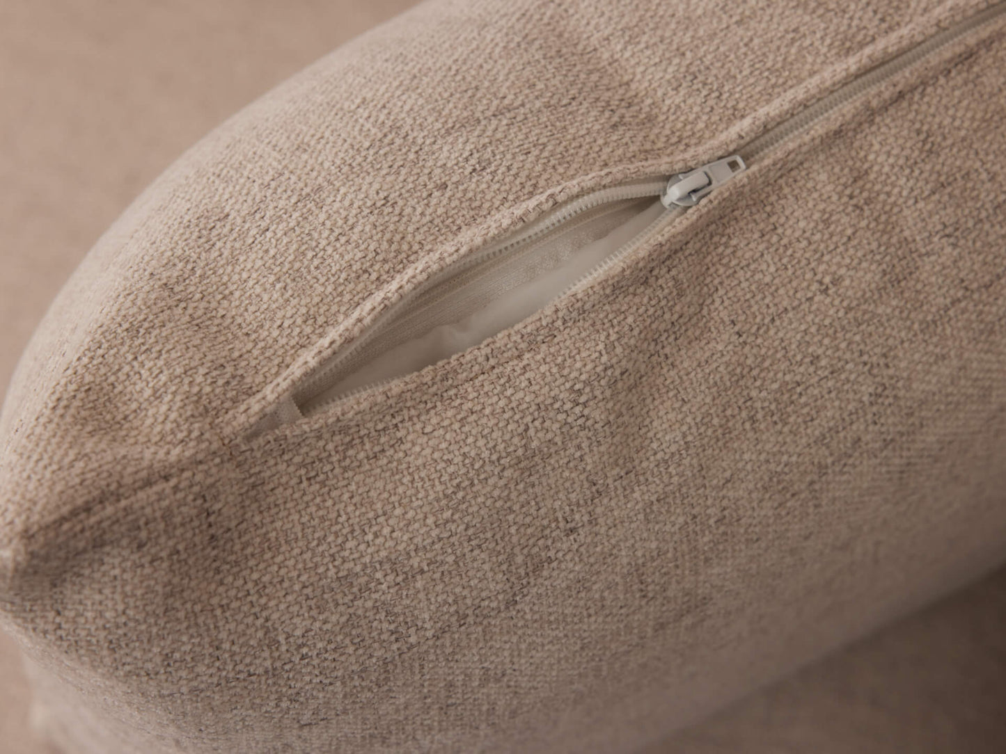 Close-up of a beige fabric cushion with a visible zipper partially open, revealing the inner filling.