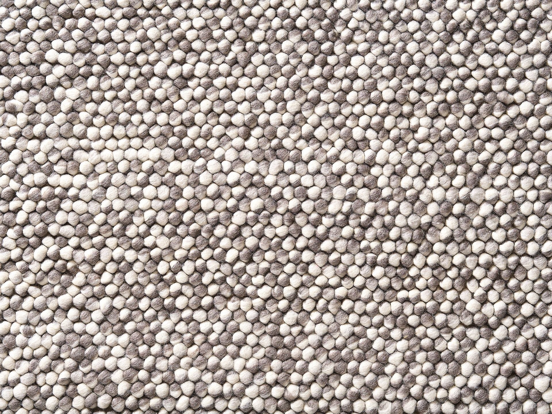 Close-up of a textured wool rug in light grey and cream, featuring a dense pebble-like pattern, creating a cosy and natural feel.
