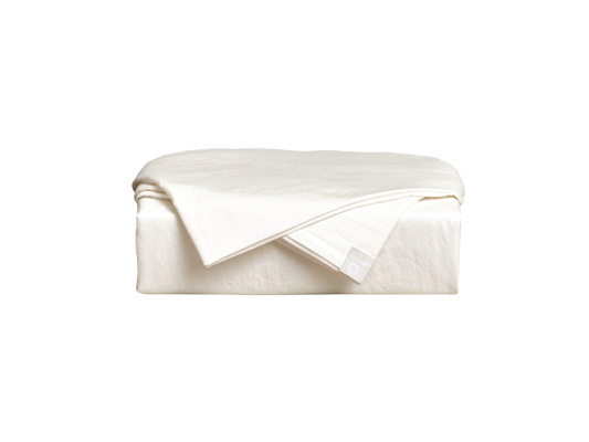 Folded cream flat sheet on a foam mattress, showcasing soft texture and a minimalist design.