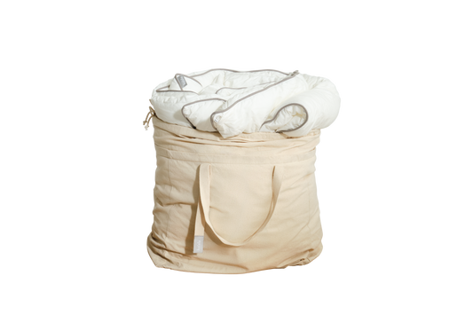 A beige fabric storage bag with handles, containing a white rolled-up quilt.