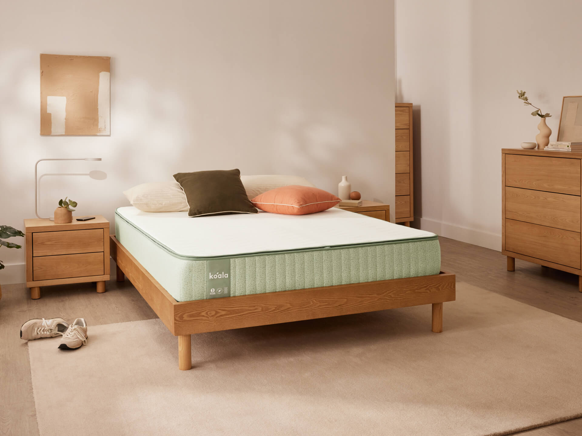 Minimalist bedroom with a light green mattress on a wooden bed frame, flanked by wooden bedside tables. Neutral tones and soft lighting.