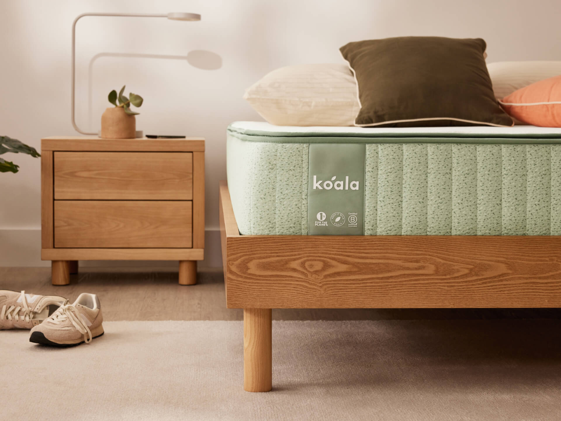 Bedroom with a wooden bed frame and mint green mattress, matching bedside table, decorative pillows, and a pair of sneakers on a light carpet.