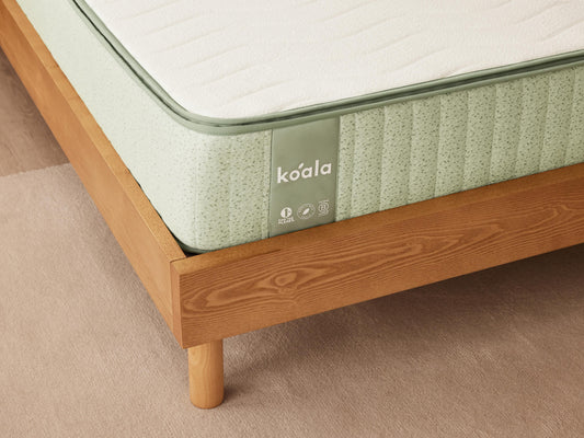 Light green mattress with a green trim on a wooden bed frame, showing the brand name "Koala".