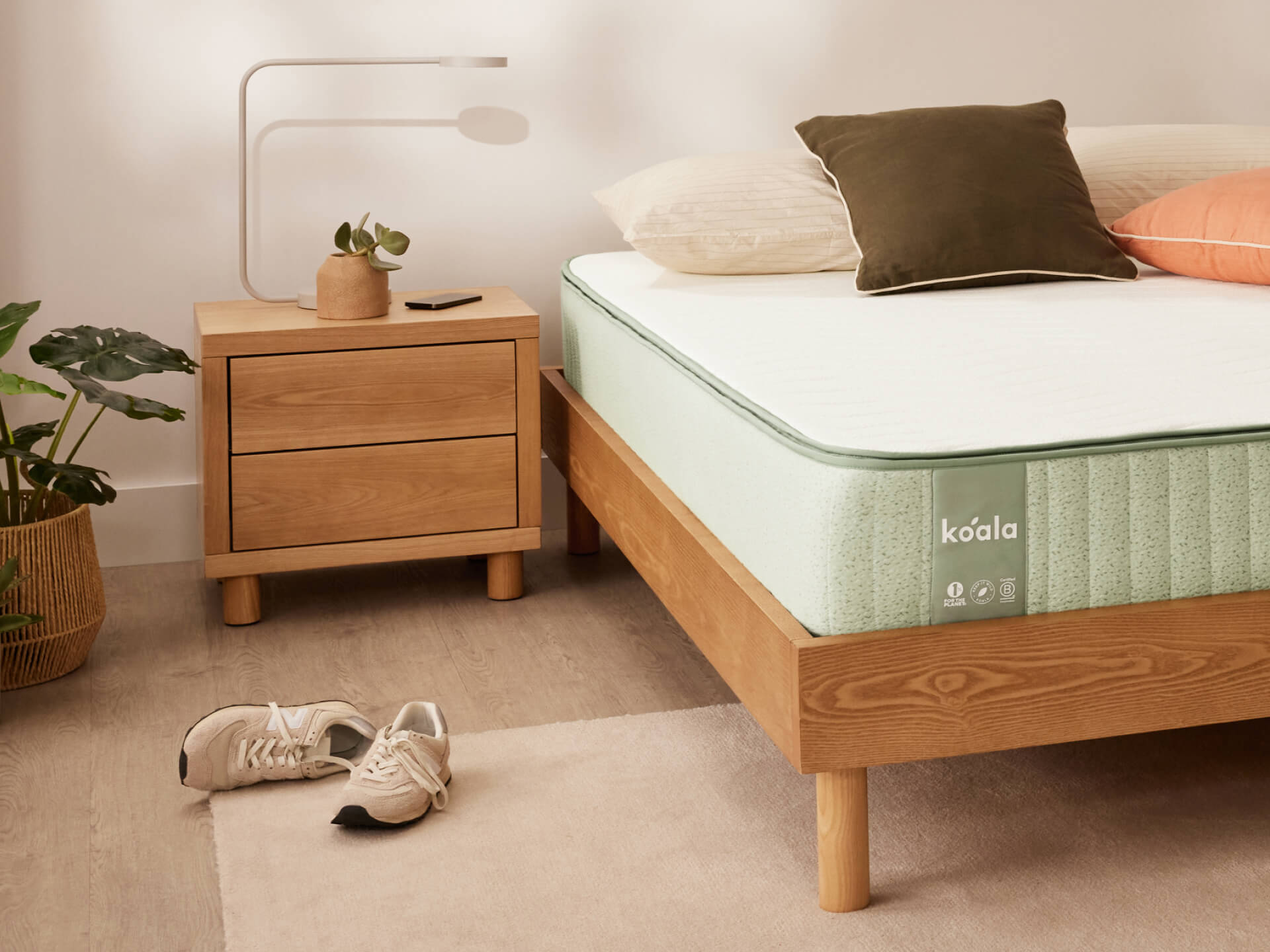 Modern bedroom with light wood bed frame and mint green mattress. Wooden bedside table with plants, and sneakers on the floor.