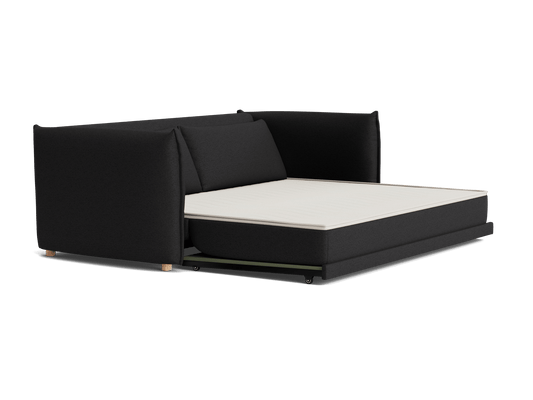 Dark grey sofa bed with extended white mattress, featuring plush cushions and wooden legs. Modern, versatile furniture piece.