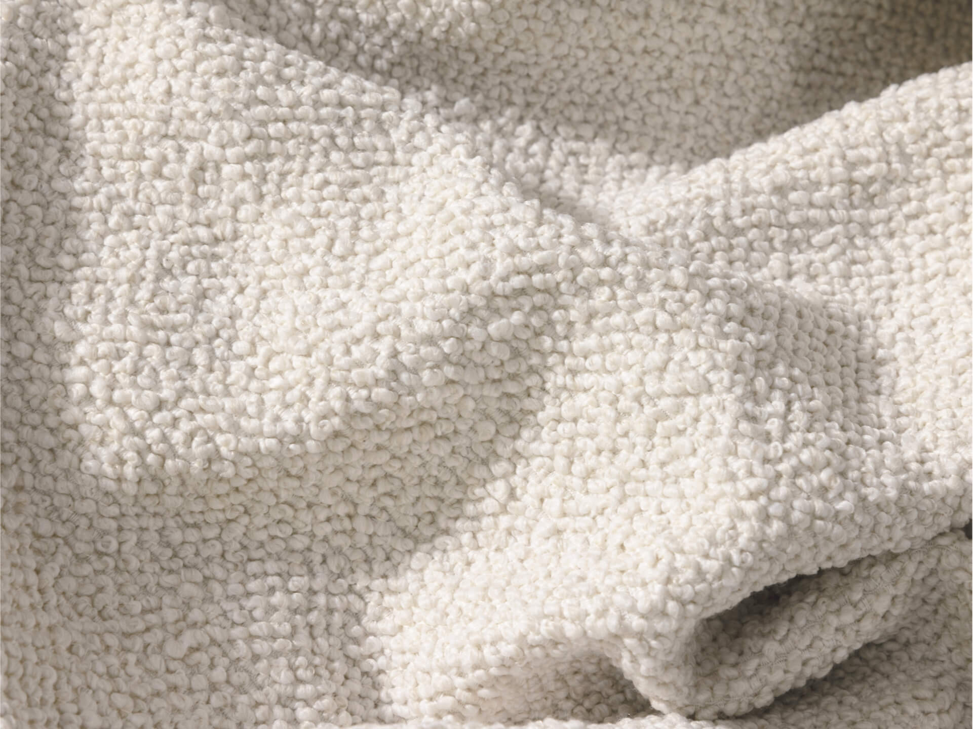 Close-up of off-white boucle fabric with a textured, looped surface, draped and softly wrinkled.