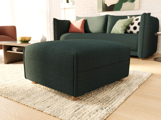 Dark green ottoman on a light beige rug in a living room with a matching dark green sofa, colourful cushions, and a wooden coffee table.