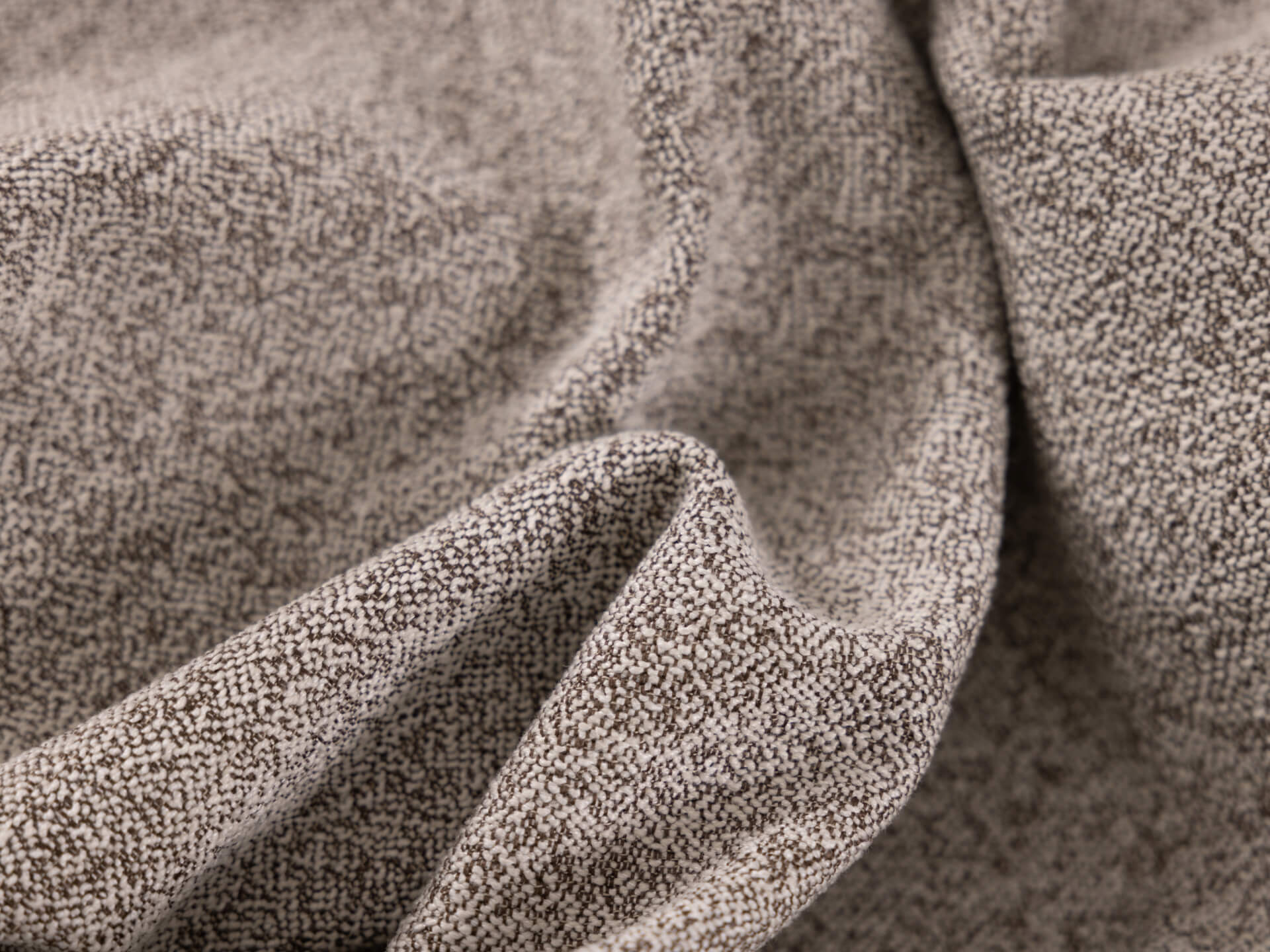 Close-up of textured light grey fabric with a speckled pattern and soft folds, suitable for furniture upholstery.