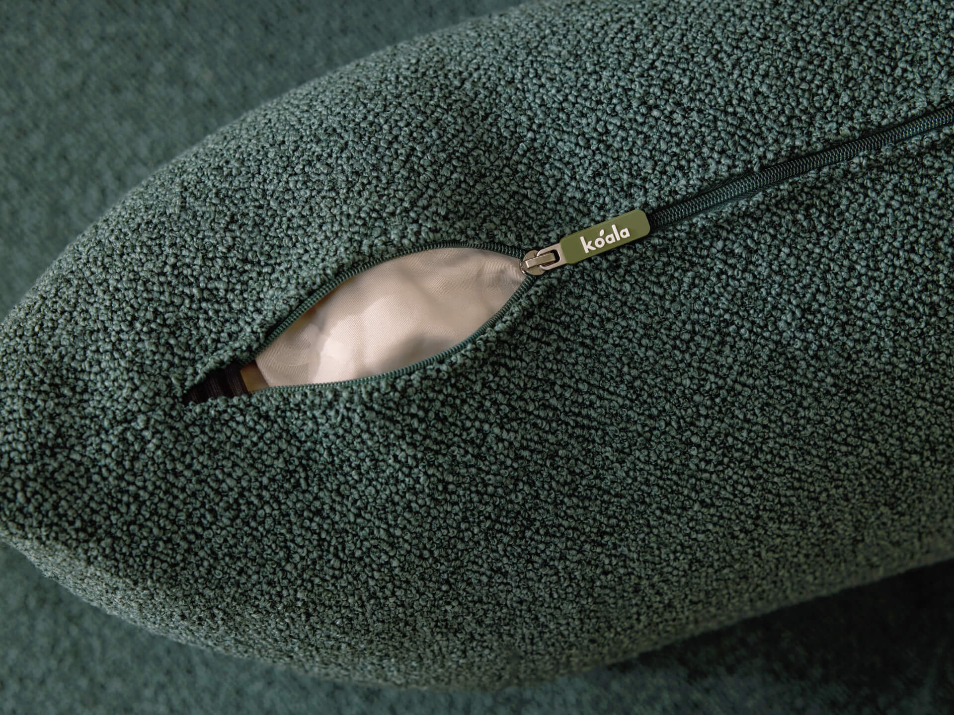 Green textured fabric cushion with a visible zip and koda tag, partially revealing inner padding.