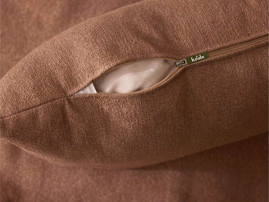 Brown textured cushion with an open zipper revealing white fabric inside, featuring a small label on the zipper pull.