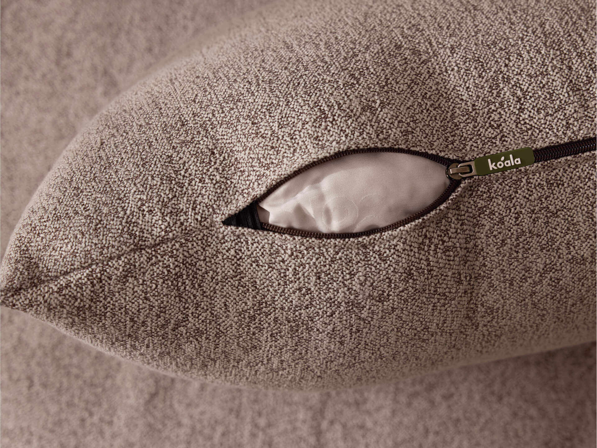 Close-up of a textured grey cushion with an open zip showing white stuffing. The zip features a small tag with branding.