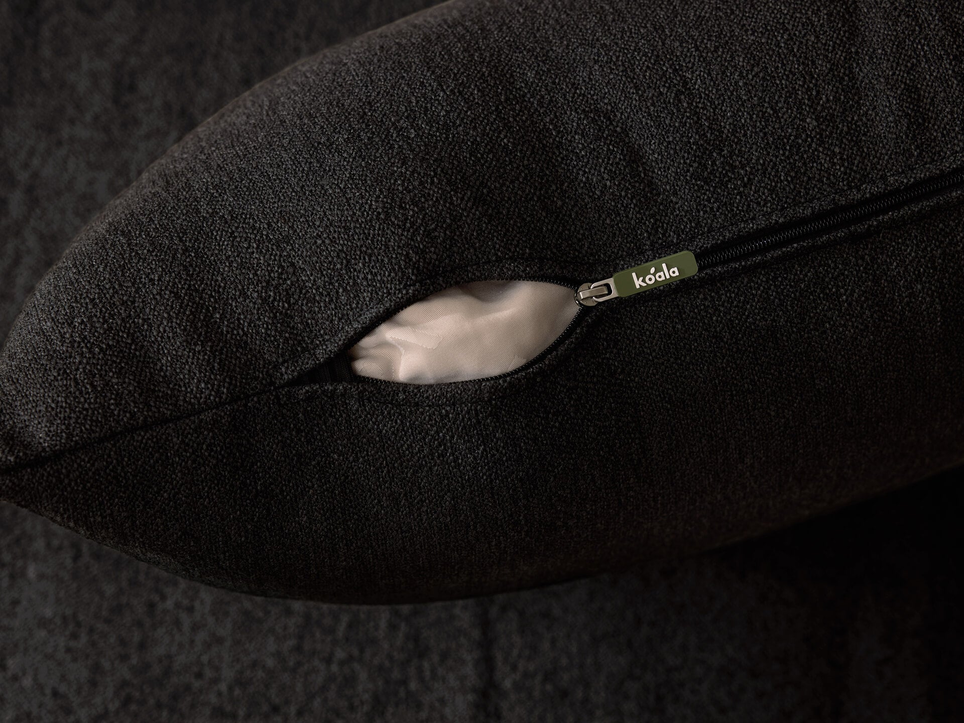 Close-up of a dark grey cushion with a visible zipper, partially open, showing the interior. The tag reads "koala".