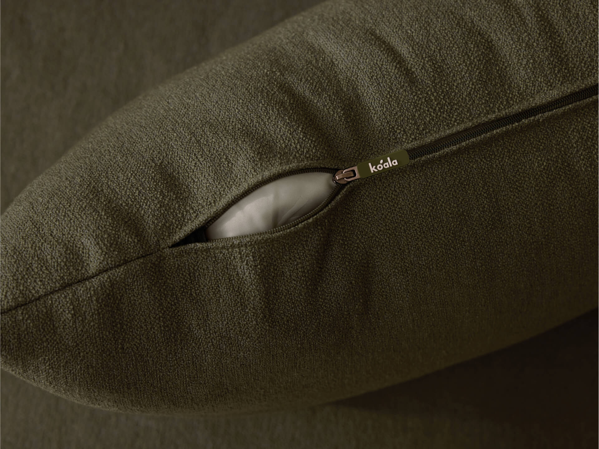 Olive green cushion with a visible zip opening, revealing the inner white filling. The fabric appears textured and soft to touch.