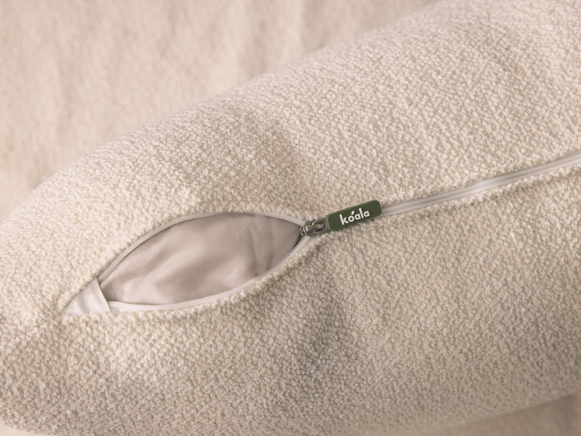 Close-up of an off-white cushion with an open zipper, revealing a white interior. A small green tag with "Koala" is attached to the zipper.