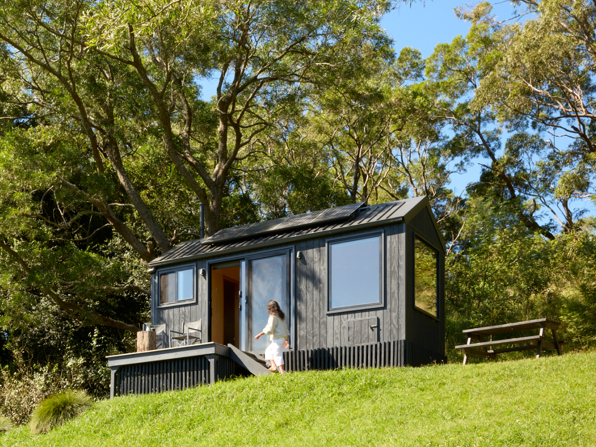 Woman stepping out of Unyoked cabin surrounded by Australian bushland and green hillside