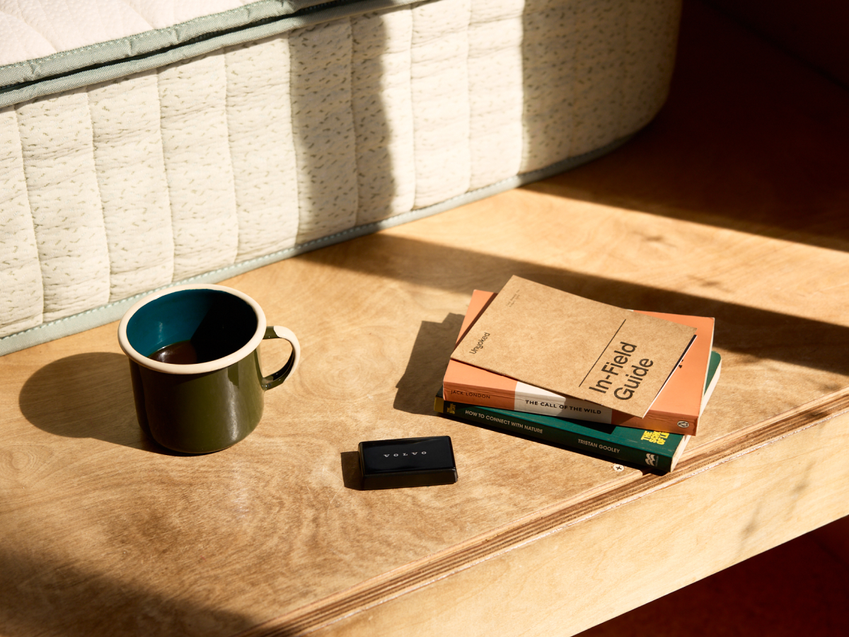 Unyoked cabin bedside with Koala mattress edge, Volvo key, books, and olive mug in morning light