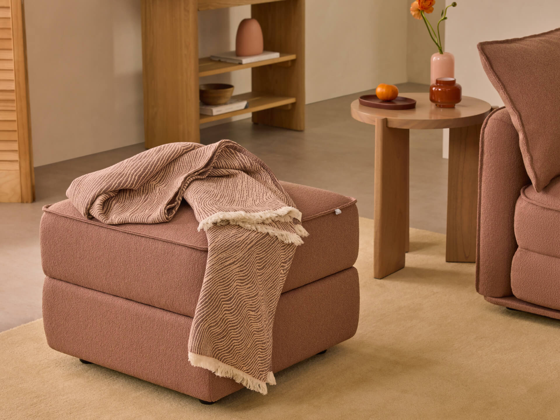 Brown ottoman with a patterned throw next to a matching sofa. Wooden side table with decor items in a cosy living room setting.